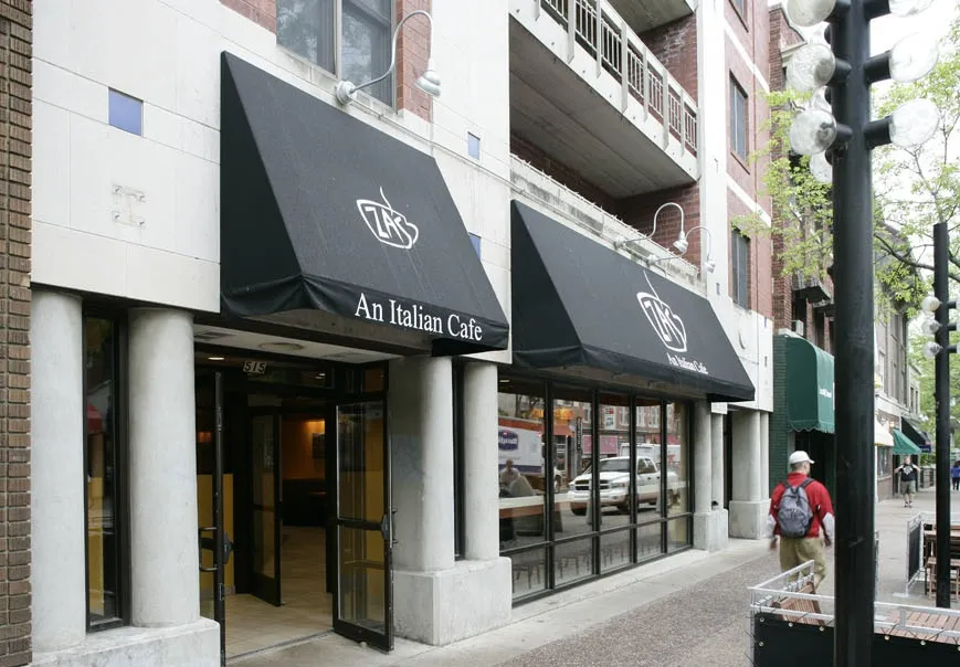 A restaurant storefront with black awnings on a downtown street